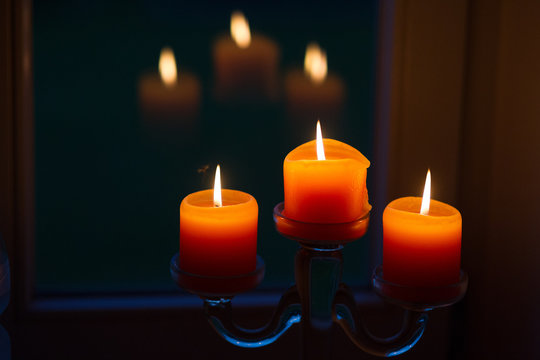 Drei Kerzen spiegeln sich in einer Fensterscheibe