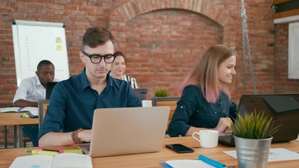 Young Team is Working in Authentic Startup Loft Red Brick Office. Business Man is Working on Laptop, Woman is Going to Discuss Project with Coworkers. 4K Static Medium Shot