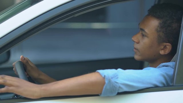 Nervous Afro-American teen boy in car getting stuck in traffic jam, driving
