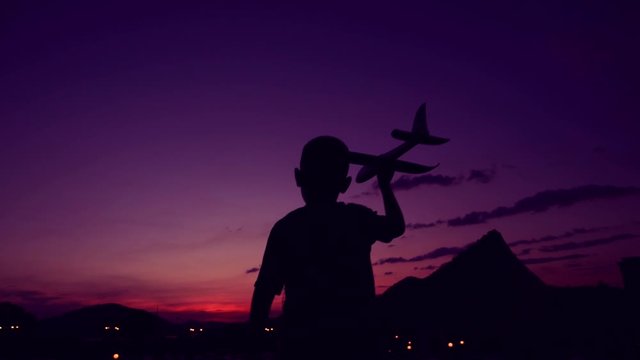 Silhouette boy playing aeroplane toy in sunset time, slow-motion