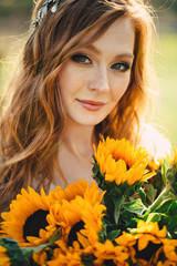 Naklejka premium portrait of a young beautiful redhead woman with a bouquet of sunflowers in sunset light