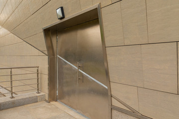 Entrance into modern building through steel door. Gray tiled concred wall surface.
