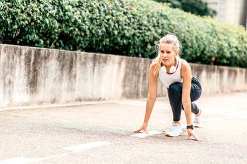 Full-length portrait of motivated woman getting ready to start running on stadium. Young sportswoman with headphones and smartwatch going to run outdoors. Summer training concept. Horizontal shot