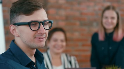 Young Happy Worker Man Discusses Ideas with his Diverse Team and Writes it down to planner. Teamwork in Loft Office. 4K Tracking Close up Corporate Shot