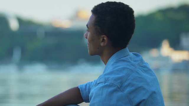 African-American teen boy throwing stones in city lake, relaxing outdoors