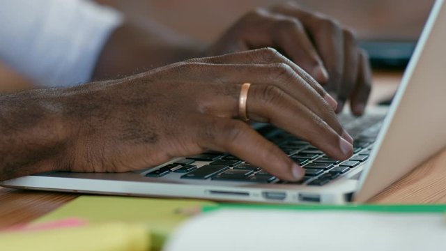 Close up to Hands of African Man Working on Laptop, Typing Text on Computer on Wooden Desk in Office or Cafe. 4K Backround Extreme Close up Shot