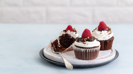 Chocolate muffins with a cup of coffee and fresh raspberries on the table, light banner, background with space text.