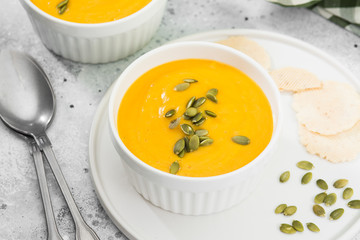 Creamy pumpkin cream soup with seeds. Autumn dish. Light grey background