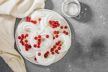Meringues in the form of rings with bunches of red currants on a white plate