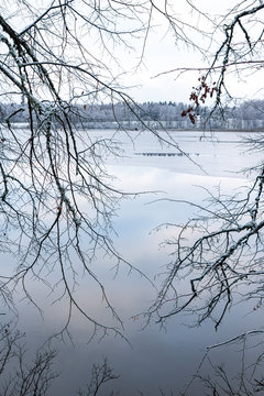 view to the lake Katvari through the tree branches in winter season with snow and ice in Latvia