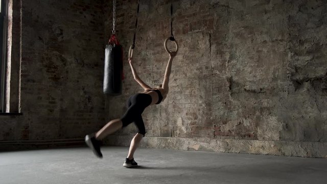 sporty girl doing flips on sports rings. Young fit woman doing stretching on gymnastic rings. Muscular young female athlete exercising with rings at gym. Young fit woman doing pull-ups on gymnastic ri