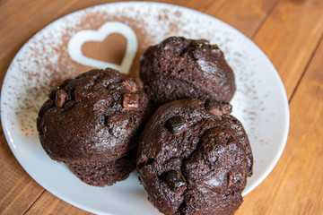 Three chocolate muffins and a heart of cocoa on a white plate.