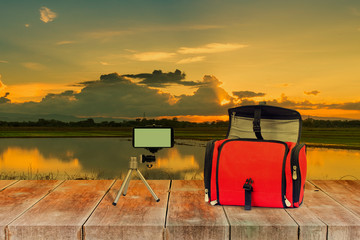 Mobile video on tripot and red bag on sunset landscape .