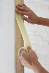 Obraz premium Man putting tape on the wall. The simple step for the quick and easy painting process. Renovation house concept. 