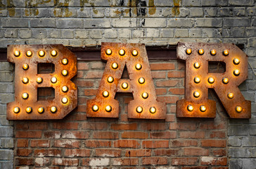 Inscription from large metal letters decorated with glowing light bulbs on the brick wall