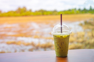 Matcha iced milk green tea on a plastic glass on woden table with nature background. Fresh and relax dring in coffee shop.
