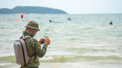 Soilder holding in his hands remote controller joystick transmitter flying the drone with sea and...