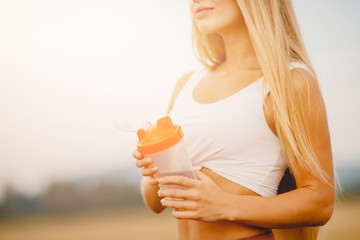 Beautiful blonde drinks water after workout in park from sports bottle