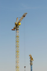 Naklejka premium A yellow high-rise building crane against a blue sky builds multi-storey apartment buildings using modern technologies of metal, concrete and brick according to an architectural project