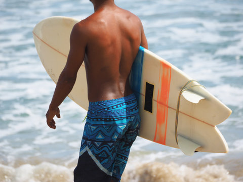 Crop image. A black surfer in shorts is getting ready to go into the ocean. Lifestyle.