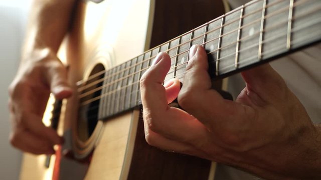 Male fingers touch the strings of an acoustic guitar close-up. Male guitarist playing music.