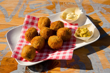White plate with bitterballen (traditional Dutch meat balls), mayonaise and mustard on a sunlit wooden table