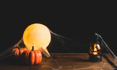 Halloween decorations with pumpkin,lantern and the moon on wooden table with a black backdrop.