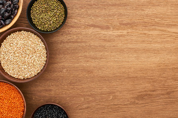 top view of bowls with black and moong beans, buckwheat and red lentil on wooden surface