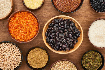 top view of bowls with beans, white rice, red lentil, couscous and buckwheat and chickpea on wooden surface