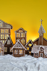 home made sweet delicious baked gingerbread village with church in front of yellow background on white snowlike velvet as traditional christmas decoration for the family