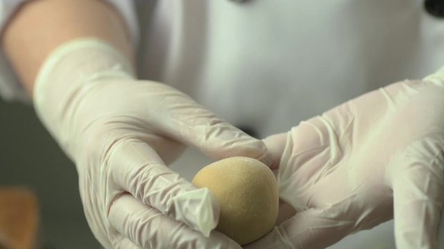 Close up of a chef hands in glove shaping rolling a round raw mooncake dough.
