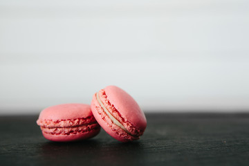Sweet colorful French macaroon cookies dessert on black stone surface over white wooden background