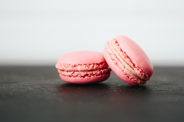 Sweet colorful French macaroon cookies dessert on black stone surface over white wooden background