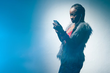 Fototapeta na wymiar African-American woman with a smartphone. A dark-skinned girl in a fur vest reads messages on her phone. African woman listening to music. Music lover girl.