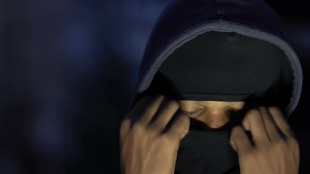 Afro-American male hooligan in hoody wearing balaclava, preparing for crime