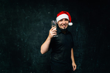 Christmas, celebration party, holiday, fun. Happy young man in Santa cap drinking champagne celebrating New Year