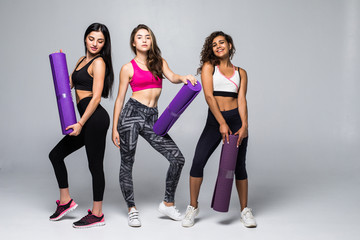 Fototapeta premium Three fitness young girls in sportswear standing isolated on white background. Girls smiling and looking to the camera.