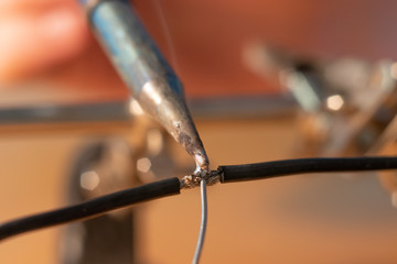Two black wires being soldered together with a soldering iron