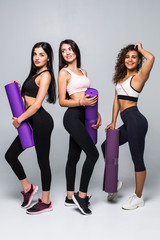 Three fitness young girls in sportswear standing isolated on white background. Girls smiling and looking to the camera.