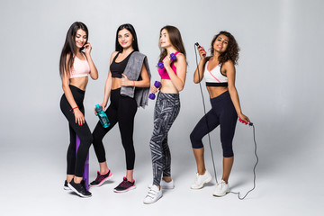 Fototapeta premium Group portrait of young sporty excited beautiful girls with exercise equipment standing beside white wall laughing and talking together. Candid funny students waiting 