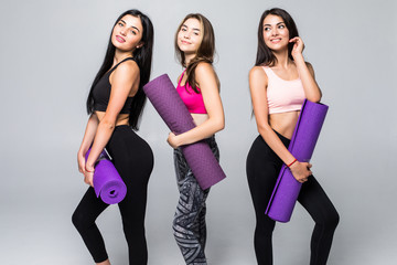Fototapeta premium Three young fitness girls holding yoga mat while standing isolated on white background