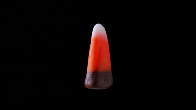 A piece of brown candy corn is seen floating and slowly rotating within a black back drop.