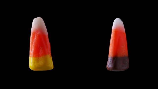 Two pieces of candy corn one brown one yellow are seen slowly spinning. Each piece of candy corn is different colored and is seen floating.