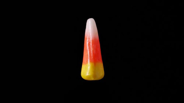 Candy corn is seen floating and slowly rotating with a dark background.