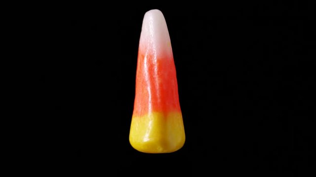 A single piece of candy corn is seen slowly rotating. The candy corn appears as if its floating and zooming back and forth to the camera.