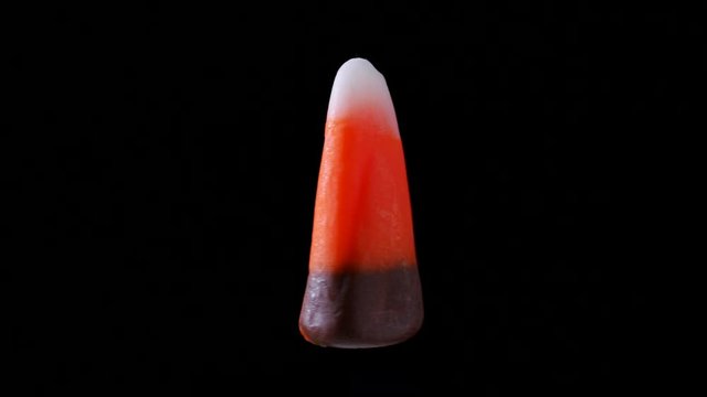 A piece of candy corn is seen floating and rotating. It is seen zooming in and out from the camera.