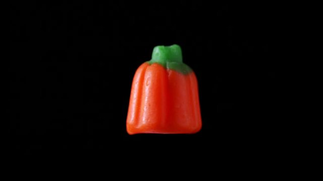 A piece of Halloween candy in the shape of a pumpkin is seen floating and rotating with a black back drop.