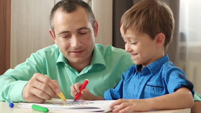 Happy family. Father and child. Dad helps his son draw with colored pencils. Relationships and fatherhood. Education.