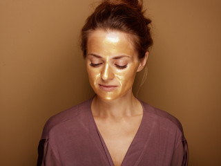 Obraz premium young housewife with golden mask isolated on bronze background
