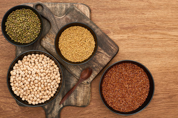 top view of bowls with moong beans, buckwheat and chickpea near spoon on wooden cutting boards
